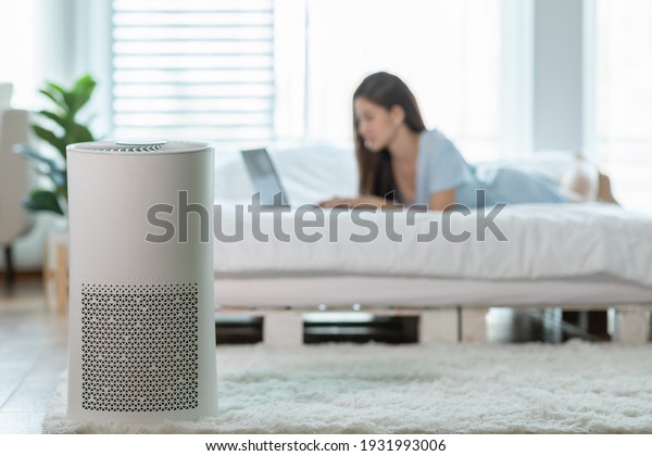 air purifier in bed room for clean dust\
and fresh air with woman lying on bed working with computer laptop\
and relax in background,Wellness of clean and fresh air for\
breathing and good health at\
home