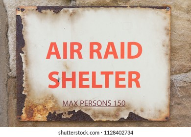 Air Raid Shelter Sign Max Persons 150 decayed old vintage warning sign with red text on rusty metal screwed to wall. World War 2 concept