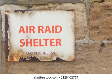 Air Raid Shelter Sign Max Persons 150 decayed old vintage warning sign with red text on rusty metal screwed to wall. World War 2 concept