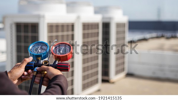 Air repair mechanic using measuring\
equipment for filling industrial factory air conditioners and\
checking maintenance outdoor air compressor\
unit.