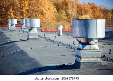 Air Roof Exhaust Ventilation Fan System Of Industrial Large Commercial Building With Hooded Chimneys Flues And Ducts In Row On Roof Top Selective Focus With Lightning Protection System.