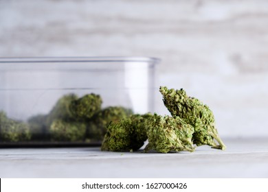 An air sealed container and recreational marijuana flower buds against a white stone background after Illinois passes a law to legalize weed sales and pardon weed related prisoners