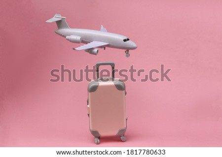 Air travel concept. Mini plastic travel suitcase, air plane on pink background.