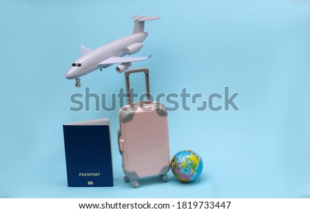Air travel concept. Mini travel suitcase, air plane, globe, passport on blue pastel background.