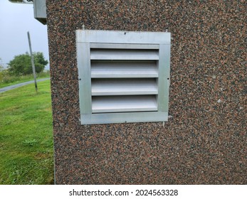 An Air Vent In The Exterior Of A Suburban Home. The Vent Has Several Slats For Air To Pass Through. It's In The Cement Foundation Of The House.