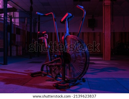 Airbike, professional exercise bike with aerodynamic loading system in pink-blue neon light in a modern health class. Cross training