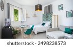 Airbnb style living room, with prepared table, big bed, convertible sofa, tv set and open window with view to sunny garden, clean and functional studio apartment in Normandy, France