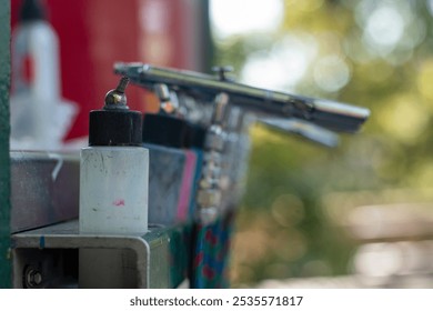 An airbrush and paint container on a workbench in a vibrant outdoor setting during daylight - Powered by Shutterstock