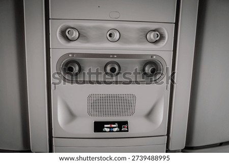 Aircraft cabin control panel includes air vents, speaker grille, and an illuminated display for passenger comfort and information in a modern airplane setting