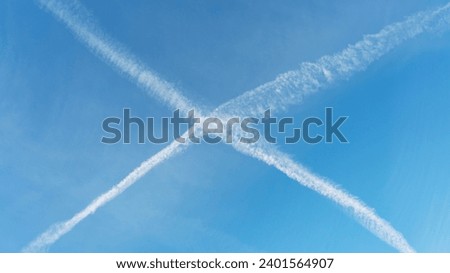 Aircraft contrails crossing and forming an X in the blue sky