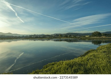 Aircraft contrails in the sky reflected in the water of an inlet early in the day - Powered by Shutterstock