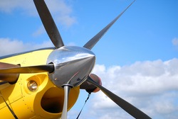 Aircraft Detail Of Prop And Spinner On Yellow Airplane.  It Is A High-performance, Five Bladed Propeller. The Engine Intake Is Positioned Directly Beneath The Prop. It Is A Sunny Day With A Few Clouds