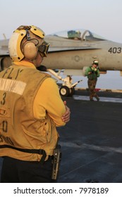 An Aircraft Director (Yellow Shirt) Awaits The Launch Of An F/A-18C Hornet On A Nuclear Aircraft Carrier, As A Catapult Crewmember (Green Shirt) Looks On