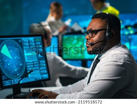 Aircraft flight control officer monitors the approach of aircraft from control tower. Air services office is equipped with navigation systems, radars and computer stations. Aviation concept.