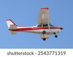 Aircraft low altitude fly by. Red and white general aviation airplane used for travel, training, and recreation. Fixed gear, high wings, and propeller powered. Isolated on blue sky