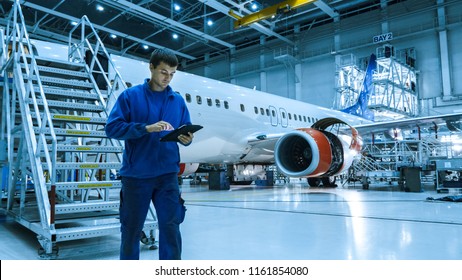 Aircraft maintenance mechanic in blue uniform is going down the stairs while using tablet in a hangar.