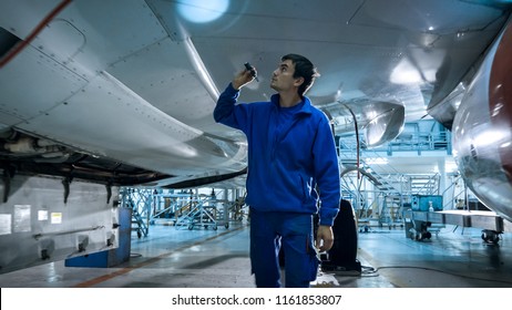 Aircraft maintenance mechanic with a flash light inspects plane fuselage in a hangar. - Powered by Shutterstock