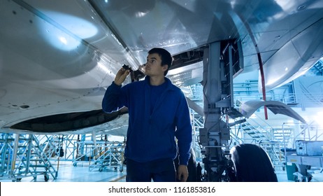 Aircraft maintenance mechanic with a flash light inspects plane fuselage in a hangar. - Powered by Shutterstock