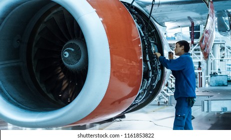 Aircraft Maintenance Mechanic With A Flash Light Inspects Plane Engine In A Hangar.