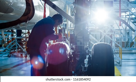 Aircraft Maintenance Mechanic With A Flash Light Inspects Plane Chassis In A Hangar.