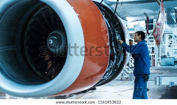 Aircraft maintenance mechanic with a flash light\
inspects plane engine in a\
hangar.