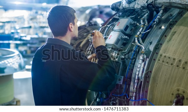 Aircraft Maintenance Mechanic Inspecting with\
Flashlight Airplane Jet Engine in\
Hangar