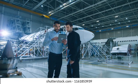 Aircraft Maintenance Worker and Engineer having Conversation. Holding Tablet.