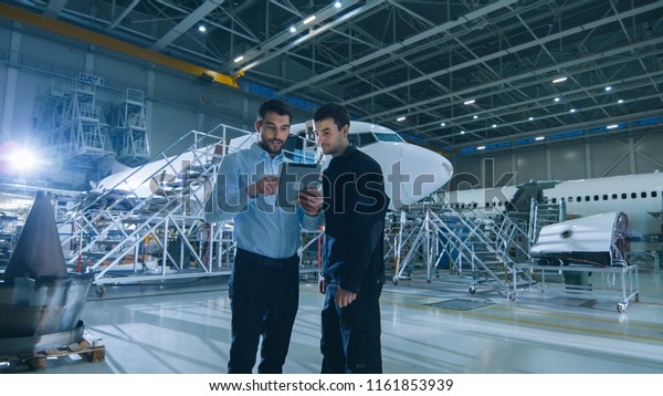 Aircraft Maintenance Worker and Engineer having
Conversation. Holding
Tablet.