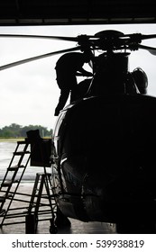 Aircraft Mechanic, Black And White  ,  Silhouette Of Helicopter With A Pilot In The Airplane Hangar. Pilot Walking Away From Helicopter Parked Outside The Hangar.