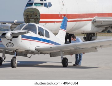 Aircraft Mechanic Inspecting A Small Engine Aircraft, Larger Airplane In Background