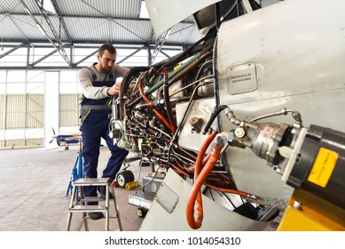 Aircraft mechanic repairs an aircraft engine in an airport hangar 