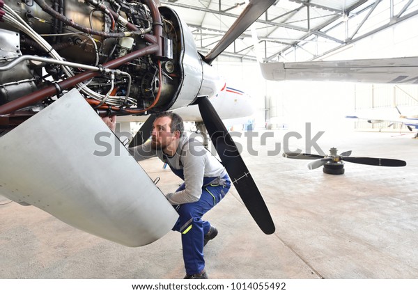 Aircraft mechanic repairs an aircraft engine in an\
airport hangar 