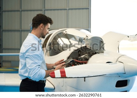 Aircraft mechanic using digital tablet performing maintenance check on small airplane engine