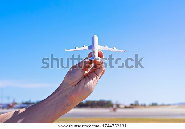 Aircraft model in hand\
against blue sky and landscape of airport. Flights ban cancelled\
concept, copy space