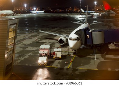 Aircraft Parked At The Airport And Preparation For Next Flight. Loading Cargo On The Plane In Airport Terminal At Night. Workers Cargo Airplane Service.