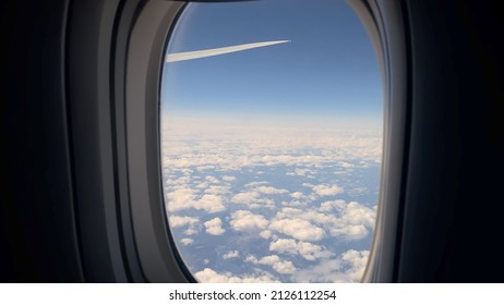 Aircraft porthole. Airplane flight, window view. Wing, blue sky and white clouds. Commercial airlines. Air travel. Tranquility, peace nature. Tourist flying to destination. - Shutterstock ID 2126112254