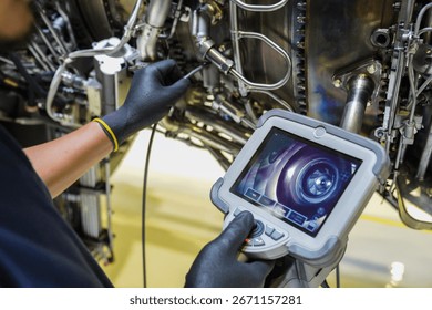 Aircraft technician using a borescope camera device to inspect the inside of a jet engine during maintenance, showing aviation technology and turbine components.