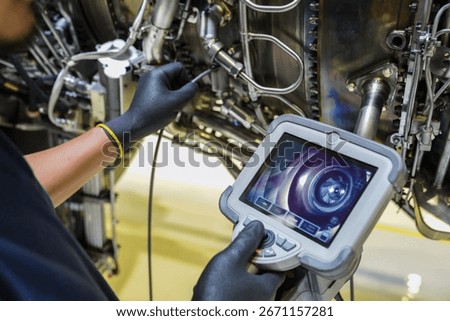 Aircraft technician using a borescope camera device to inspect the inside of a jet engine during maintenance, showing aviation technology and turbine components.