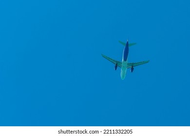 Aircraft In White And Blue Color Against The Blue Sky. Passenger Air Transportation. Airplane Silhouette From Below.