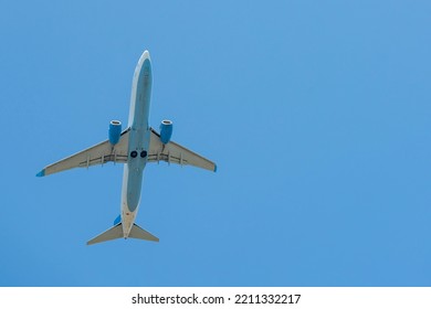 Aircraft In White And Blue Color Against The Blue Sky. Passenger Air Transportation. Airplane Silhouette From Below.