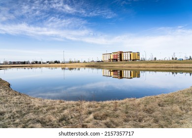 Airdrie Alberta Canada, May 06 2022: A Storm Water Retention Pond For Run Off In A Commercial Area With A Days Inn Suits Early Morning Reflection.