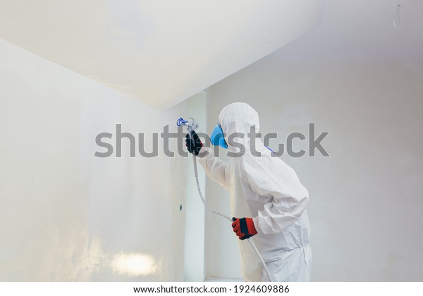 Airless spray paint. The worker\
paints the wall with an airless spray in white, an experienced\
worker sprays the paint on the surface with a mechanical air\
tool