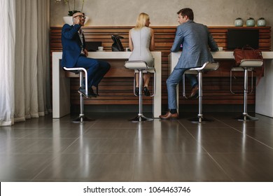 Airline passengers sitting at free internet service counter in airport. People at internet cafe inside airport terminal. - Shutterstock ID 1064463746
