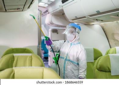 Airline Woman Staff In Protective Suit (PPE) Wearing Medical Face Mask Disinfecting Spray For Covid-19 Or Coronavirus At Airplane Cabin After Or Before Landing Or Take Off To Disease Prevention