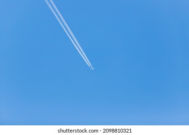 Airliner in the blue sky without clouds. There are engine tracks behind the plane.
