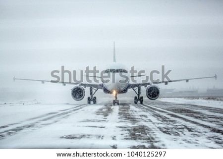 Airliner on runway in blizzard. Aircraft during taxiing at heavy snow. Passenger plane in snow at airport. Modern twin-engine passenger airplane taxiing for take off at airport during snow blizzard