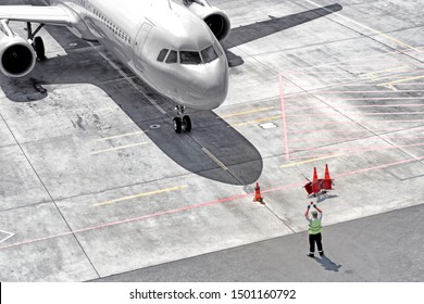 Airplane Arrival To Airport Runway Aerial Top Down Front Closeup View Of Modern Passenger Plane Arriving To Terminal Gate With Maintenance Worker Person Guiding To Park Aircraft For Disembarkment