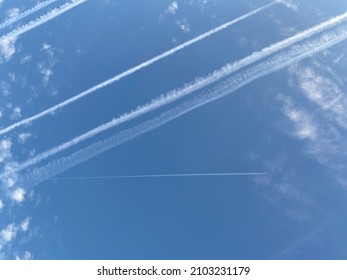 Airplane in the blue sky with clouds from below. High flying passenger plane with condensation trail. Jets flying overhead diagonally in sky with sunlight. Bottom view.