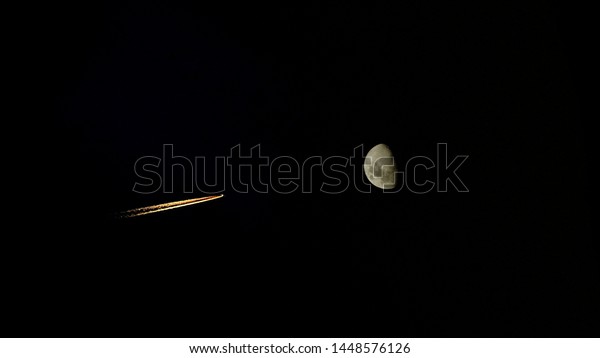 Airplane contrails and\
half moon at night