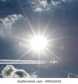 An Airplane Creating Jet Stream Trail Across A Bright Shining Sun.
